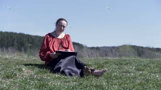 Woman sketching in a park sitting on the short green grass under the summer sunlight. Clip. Female