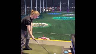 big brother hitting golf ball at topgolf