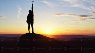 Aerial view of a silhouette of a woman standing on the top of a mountain happily waving her hands