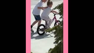 It's a lovely sibling moment. Brother teaching his sister how ride a bike.