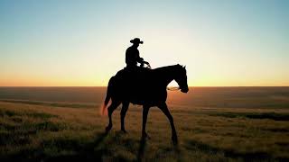 A lone cowboy rides his horse across an open plain at beautiful sunset, soft light, warm colors