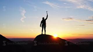 Silhouette of a female climber celebrating victory at the top of the mountain at sunset