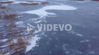 Aerial birdseye view of frozen lake Liepaja during the winter, blue ice with cracks, dry yellowed re