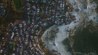 Aerial birds eye overhead top down view of big waves rolling on sea coast  buildings in reside