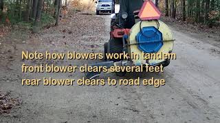 Two debris blowers clearing road of accumulated leaves