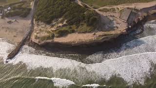 Ascending aerial top down shot of gigantic coastline cliffs with reaching waves from the ocean