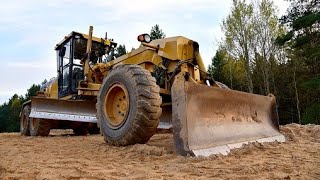 A large yellow grader is cutting plants along the wall of an alley