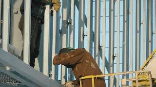 Industrial worker welding high at the construction site in daytime. Sparks fly as one welder welds