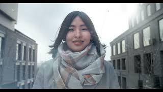 Asian woman stands between business buildings and looks at the camera. Winter sun. lens flares.