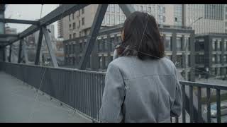 An Asian girl walks along a bridge crossing against the backdrop of an industrial, business