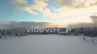 Aerial pullback, frozen lake covered with thick snow during winter season in pine forest during dawn