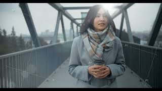 A young beautiful Asian woman in a coat with a cup of coffee walks along the bridge, smiles