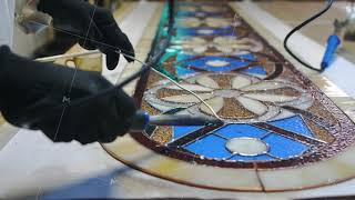 Soldering stained glass seams. Gloved artist's hands with a soldering iron. Stained glass workshop