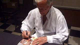 Pat Boone signing autographs on several records