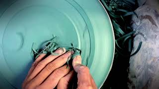 Trimming a green stoneware plate on the pottery wheel